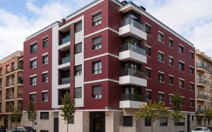 Edificio residencial de cinco alturas en esquina con fachada de acabado continuo en granate, bandas blancas horizontales, balcones volados en color blanco y zócalo aplacado en planta baja.