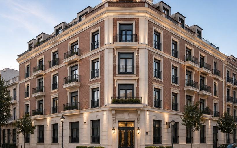 Edificio clásico de cinco alturas en esquina con paños de ladrillo, aplacado de piedra clara en zócalo, cornisas, recercados y esquinas, balcones de forja y portal iluminado en el chaflán.
